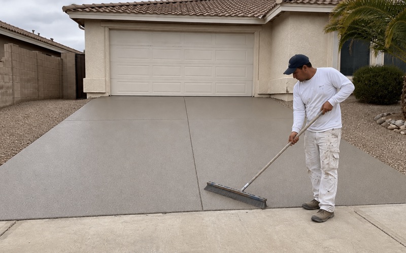 A finisher kneels with a flat palm on a sand-colored textured pool deck coating at the bullnose coping curb.